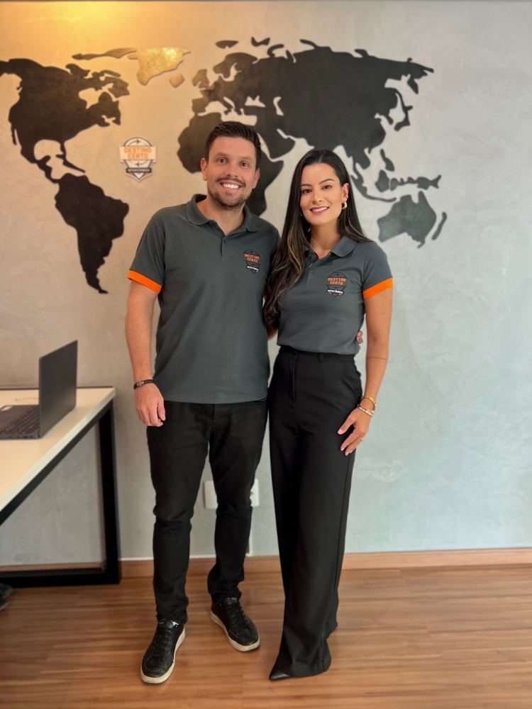 Os fundadores da Destino Certo Intercâmbios, de camisa da agência, em frente ao mapa-múndi do escritório em Campo Belo